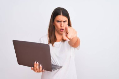 Bilgisayarla çalışan güzel genç bir kadın beyaz arka plan üzerinden kızgın ve hayal kırıklığına uğramış bir şekilde kameraya işaret ediyor.