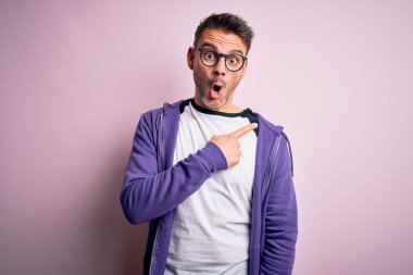 Pembe arka planda duran mor eşofman üstü ve gözlüklü genç yakışıklı adam..