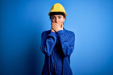 Mavi gözlü, güvenlik kaskı takan ve üniforma giyen genç ve güzel bir işçi kadın yanlışlıkla ağızlarını kapatarak şok geçirdi. Gizli konsept.