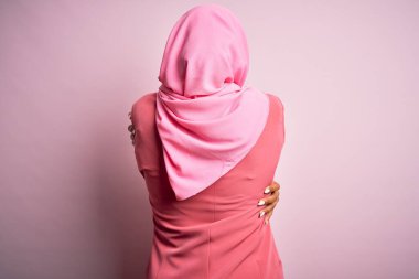 İzole edilmiş pembe arka planda Müslüman tesettürlü genç Afro kadın mutlu ve pozitif bir şekilde kendine sarılıyor. Sevgi ve özgüven.