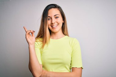 Güzel, mavi gözlü, yeşil tişörtlü, beyaz arkaplanlı, yüzünde kocaman bir gülümseme olan, elleri ve parmakları kameraya bakan sarışın bir kadın..