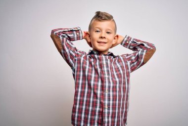 Mavi gözlü, zarif gömlekli küçük beyaz çocuk izole edilmiş arka planda duruyor rahatlıyor ve esniyor, kolları ve elleri başının arkasında mutlu bir şekilde gülümsüyor.