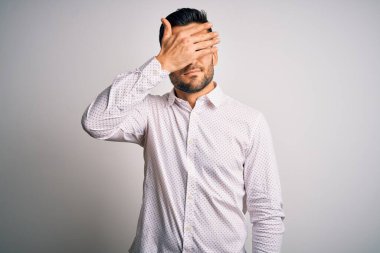 Zarif bir gömlek giyen yakışıklı bir adam soyutlanmış beyaz arka planda duruyor. Gözleri elle kaplıyor, ciddi ve üzgün görünüyor. Görme, saklama ve reddetme konsepti