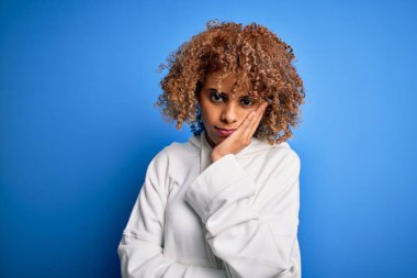 Güzel Afro-Amerikan spor kadını mavi arka plan üzerine sıradan bir kazak giyiyor. Kollarını kavuşturup depresyondan sıkılmış ve yorgun görünüyor..