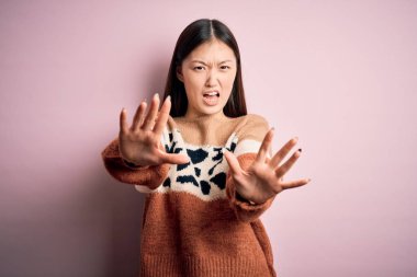 Pembe izole edilmiş arka planda hayvan desenli süveter giyen genç, güzel Asyalı kadın korku ifadesinden korkuyor ve dehşete düşüyor. El hareketlerini durdur, şok içinde bağır. Panik konsepti.