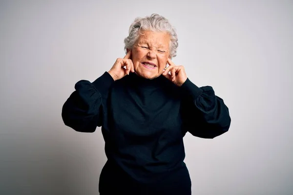 年长的漂亮女人穿着宽松的黑色毛衣 站在孤立的白色背景之上 用手指捂住耳朵 对嘈杂的音乐感到恼怒 聋人概念 — 图库照片