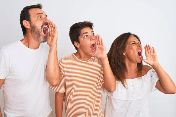 Family of three, mother, father and son standing over white isolated background shouting and screaming loud to side with hand on mouth. Communication concept.