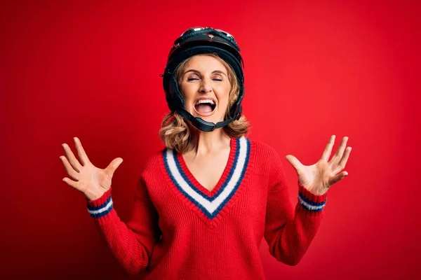 赤の背景に元ヘルメットをかぶっている中年の美しいブロンドのオートバイの女性が狂った叫びと積極的な表情と腕を上げて叫んでいます 欲求不満の概念 — ストック写真