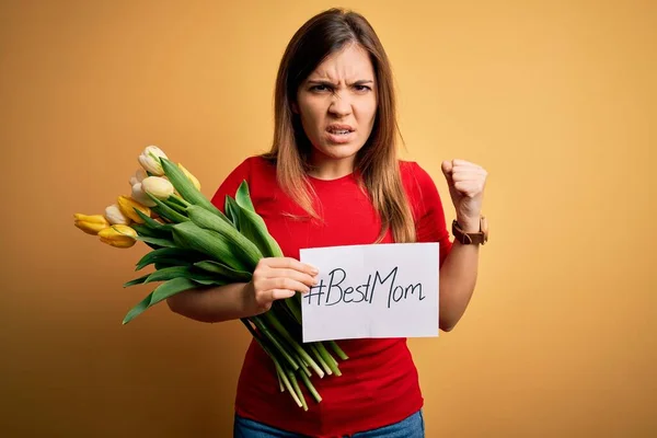 Beautiful woman holding paper with best mom message and tulips celebrating mothers day annoyed and frustrated shouting with anger, crazy and yelling with raised hand, anger concept
