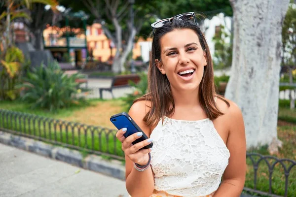 夏の晴れた日に街を歩いて幸せな笑顔の若い美しい女性スマートフォンを使用して — ストック写真
