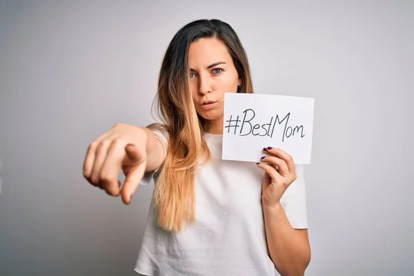 Young beautiful woman holding paper with best mom message celebrating mothers day pointing with finger to the camera and to you, hand sign, positive and confident gesture from the front