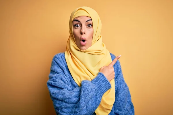 年轻美丽的黑发女穆斯林 头戴阿拉伯头巾 头戴黄褐色头巾 手指指向侧面 张开嘴 惊讶的表情 — 图库照片
