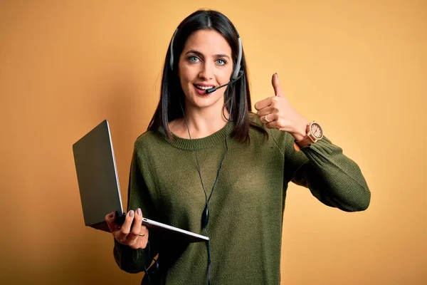 Young operator woman with blue eyes working on call center using computer laptop and headset happy with big smile doing ok sign, thumb up with fingers, excellent sign