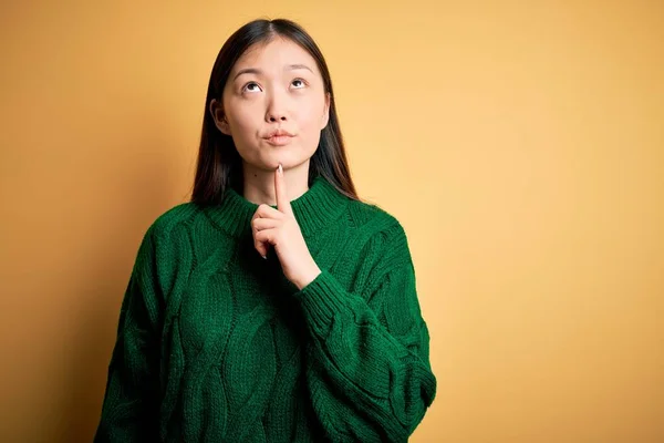 녹색의 스웨터를 배경을 아름다운 아시아 손가락을 올려다보며 의심하는 했습니다 — 스톡 사진