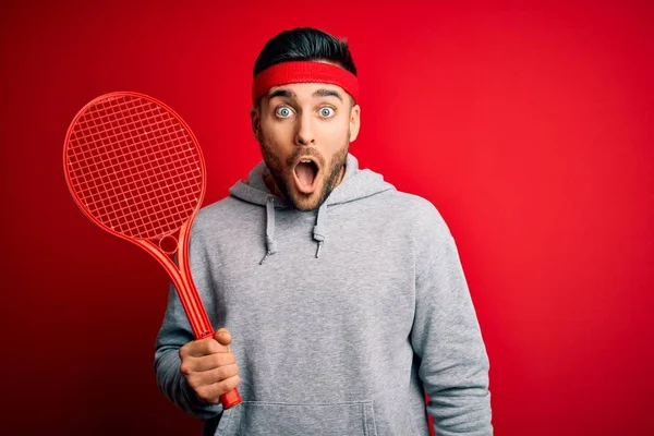 Junger Gutaussehender Sportler Mit Tennisschläger Sportbekleidung Über Rotem Hintergrund Erschrocken — Stockfoto