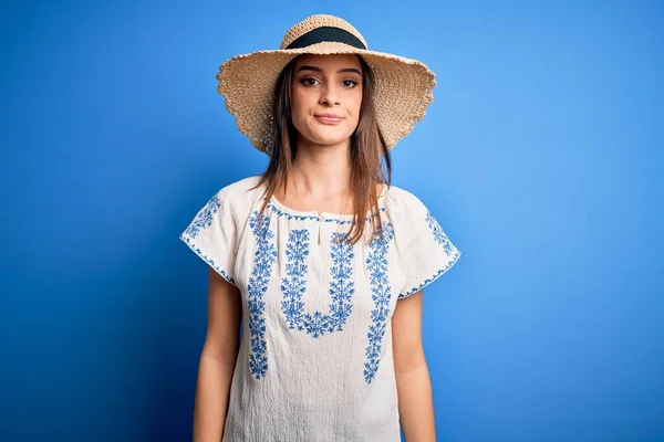 顔に真剣な表情で青の背景にカジュアルなTシャツと夏の帽子を身に着けている若い美しいブルネットの女性 シンプルで自然なカメラを見て — ストック写真