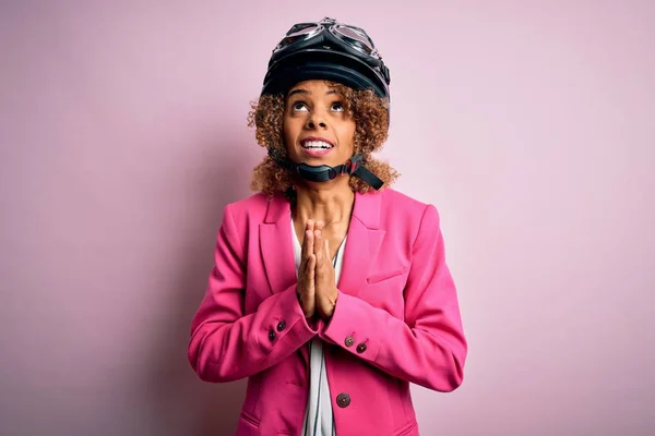 ピンクの背景に元ヘルメットを身に着けている巻き毛を持つアフリカ系アメリカ人のオートバイの女性は懇願し 顔に希望の表現と一緒に手で祈る非常に感情的かつ心配 物乞い — ストック写真
