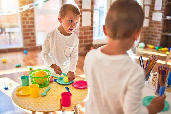 Adorable blonde twins playing around lots of toys. Cooking plastic food toy at kindergarten