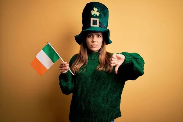 英俊潇洒的女人头戴绿帽 头戴爱尔兰国旗 在圣帕特里克节庆典上举着爱尔兰国旗 满脸怒容 脸上挂着厌恶大拇指的负面标志 被拒绝的念头 — 图库照片