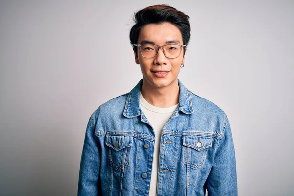 Young handsome chinese man wearing denim jacket and glasses over white background with a happy and cool smile on face. Lucky person.