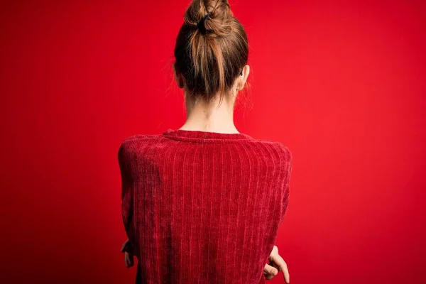 年轻美丽的红头发女人 穿着宽松的毛衣 站在孤立的红色背景上 背对着前方 交叉着双臂 — 图库照片
