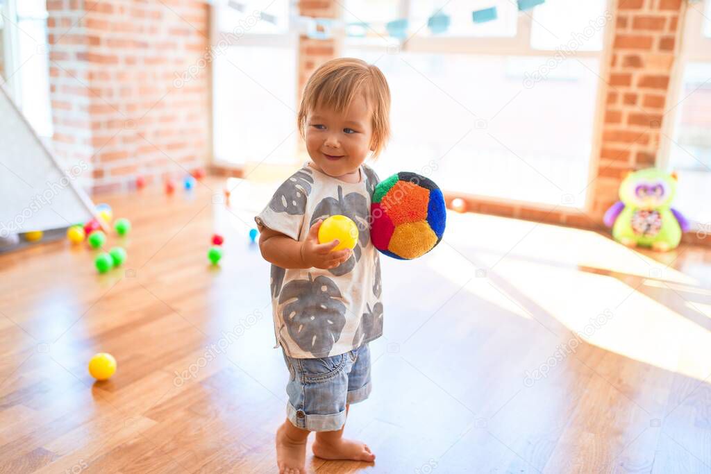 Adorable toddler playing with balls around lots of toys at kindergarten