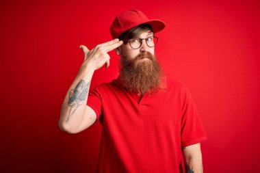 Gözlüklü ve kırmızı şapkalı genç teslimatçı izole edilmiş arka planda kendini vuruyor ve öldürüyor silah gibi el ve parmakları işaret ediyor, intihar jesti..