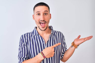 Deniz çizgili tişört giyen genç bir adam izole edilmiş arka planda durup hayrete düşmüş ve kameraya gülümserken eliyle ve parmağıyla işaret ediyordu..