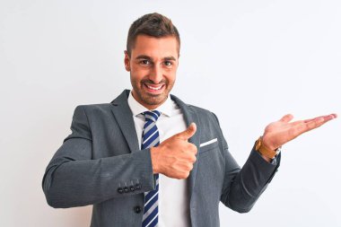 Takım elbiseli ve kravatlı genç yakışıklı iş adamı avuç içini gösteriyor ve baş parmaklarıyla iyi bir hareket yapıyor, mutlu ve neşeli gülümsüyor.