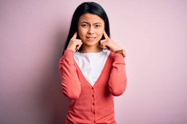 Gürültülü müzik sesi için pembe arka plan üzerine günlük süveter giyen genç, güzel Çinli bir kadın kulaklarını parmaklarıyla kapatıyor. Sağır kavramı.