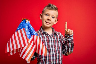Kırmızı arka planda Usa bayrağı taşıyan küçük Amerikalı vatansever beyaz çocuk bir fikir ya da soruyla şaşırdı ve mutlu bir yüzle işaret etti.