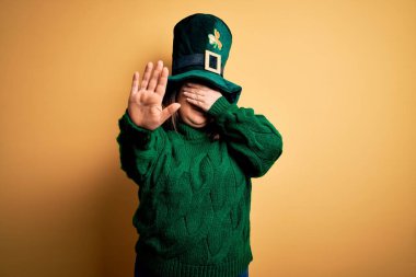 Genç, iri yarı, yeşil şapkalı ve yonca takan genç bir kadın Aziz Patrick Günü 'nü kutluyor gözleri ellerle kapıyor ve üzgün ve korku ifadeleriyle jestleri durduruyor. Utanç verici ve olumsuz bir kavram..