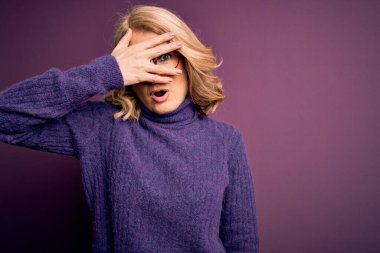 Orta yaşlı, sarışın, sıradan mor balıkçı yaka kazak giyen, gözlüklü, yüzü ve gözleri kapalı, utangaç bir ifadeyle parmaklarından bakan güzel bir kadın..