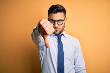 Sarı arka plan üzerinde duran kravat ve gözlük takan genç yakışıklı işadamı mutsuz ve kızgın görünüyor. Reddedilmiş ve olumsuz. Kötü ifade.