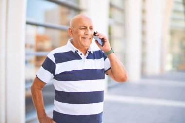 Kıdemli yakışıklı adam mutlu ve kendinden emin gülümsüyor. Yüzünde gülümsemeyle kasaba caddesinde telefonla konuşuyor.