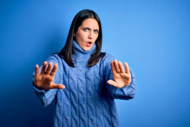 Mavi gözlü, balıkçı yaka kazak giyen genç esmer kadın avuçlarıyla jestleri durduruyor, sinirli ve hüsran dolu bir ifade takınıyor.