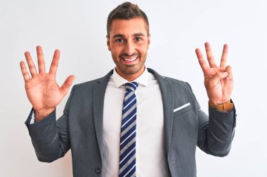 Takım elbiseli ve kravatlı genç yakışıklı iş adamı 8 numaralı parmaklarıyla gülümseyerek kendinden emin ve mutlu olduğunu gösteriyor..
