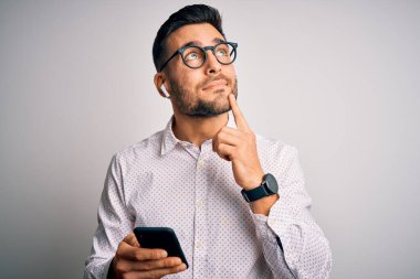 Gözlük takan yakışıklı genç adam akıllı telefon ve kulaklık kullanarak konuşuyor. Ciddi bir yüz ifadesi var. Soru soruyor, kafası karışık bir fikir.