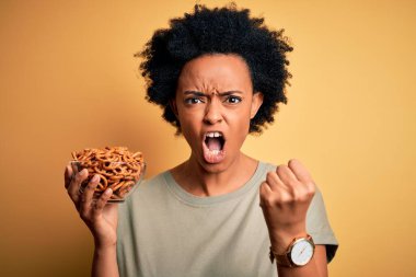 Kıvırcık saçlı, fırında Alman krakerleri olan Afro saçlı genç bir Afro kadın öfkeyle bağırıyor, deliriyor ve el kaldırarak bağırıyor.