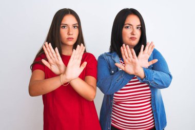 İzole edilmiş beyaz arka plan üzerinde duran gündelik giysiler giyen genç ve güzel kadınlar reddedilme ifadesi kollarını ve avuç içlerini çaprazlayarak negatif işaret veriyorlar, kızgın yüz ifadesi takınıyorlar.