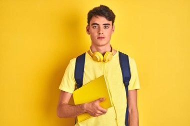 Kulaklık takan ve sırt çantası takan genç bir çocuk izole edilmiş bir arka planda kitap okuyor.