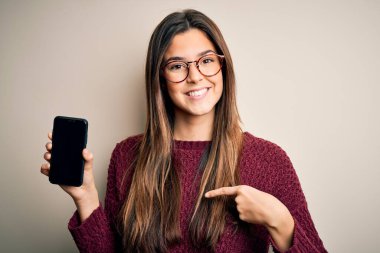 Gözlük takan genç ve güzel bir kız izole edilmiş beyaz arka planda akıllı telefon gösteriyor.