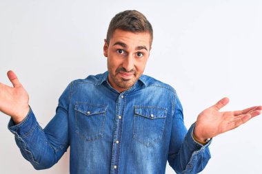 Kotlu ceket giyen genç yakışıklı adam izole edilmiş arka planda duruyor. Kolları ve elleri havada, kafası karışmış bir ifade takınıyor. Şüphe kavramı.