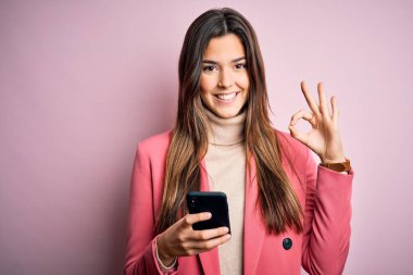 Genç ve güzel bir kız beyaz arka plan üzerinde akıllı telefon kullanarak konuşuyor tamam işareti yapıyor, mükemmel bir sembol.