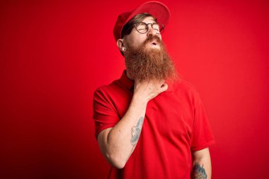 Gözlüklü yakışıklı teslimatçı ve izole edilmiş arka planda kırmızı şapkalı. Ağrılı boynuna dokunuyor. Grip, mantar ve enfeksiyon yüzünden boğazı ağrıyor.