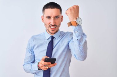 Genç ve yakışıklı iş adamı, izole edilmiş arka planda akıllı telefon kullanıyor. Sinirli ve sinirli bir şekilde bağırıyor, çıldırıyor ve el kaldırarak bağırıyor.