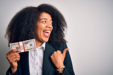 Afro saçlı Afrikalı Amerikalı genç bir iş kadını elinde bir sürü nakit para banknotları var. Başparmağıyla gülümsüyor ve onu işaret ediyor.
