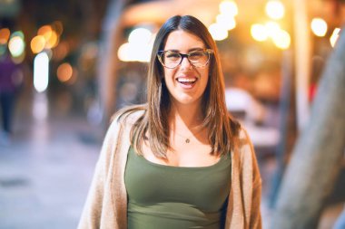 Mutlu ve kendinden emin gülümseyen genç ve güzel bir kadın. Kasaba caddesinde yüzünde gülümsemeyle dikilirken