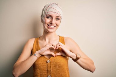 Genç, güzel, kızıl saçlı, kazara yaralanmış, kafasında bandaj olan, sevgiyle gülümseyen, kalp sembolü ve şekli ellerle beliren bir kadın. Romantik konsept.