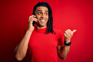 Afrika kökenli Afro Amerikalı genç adam Rastalı saçlarıyla akıllı telefondan konuşuyor ve gülümseyen bir gülümsemeyle baş parmağını kaldırıyor.